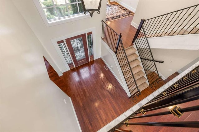 foyer entrance featuring a towering ceiling, baseboards, stairway, visible vents, and wood finished floors
