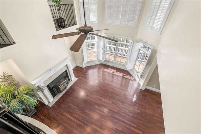 unfurnished living room featuring wood finished floors, a high ceiling, a ceiling fan, and a healthy amount of sunlight