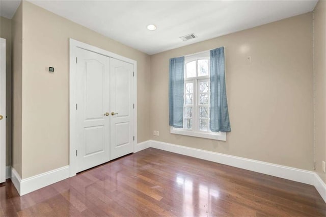 unfurnished bedroom featuring a closet, visible vents, baseboards, and wood finished floors