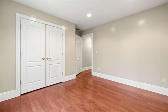 unfurnished bedroom with a closet, baseboards, recessed lighting, and wood finished floors