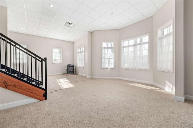 unfurnished living room with visible vents, a wood stove, carpet floors, and baseboards