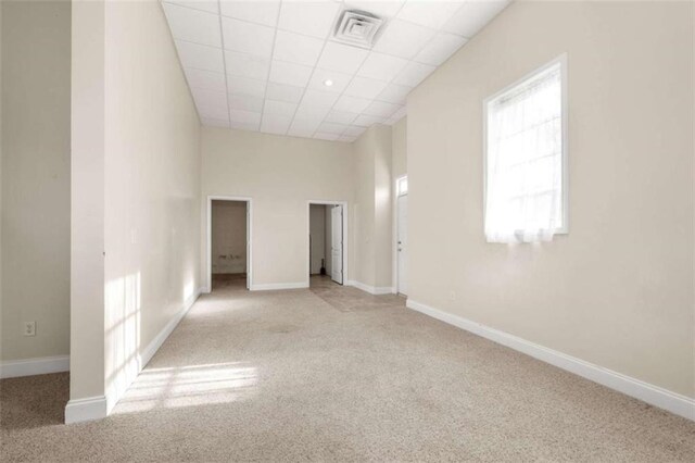 carpeted empty room featuring visible vents, baseboards, and a drop ceiling