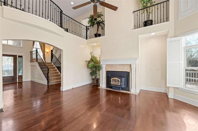 unfurnished living room featuring plenty of natural light, ceiling fan, a towering ceiling, and dark wood-type flooring