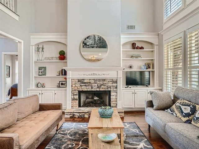 living room with built in shelves, dark hardwood / wood-style floors, a stone fireplace, and plenty of natural light