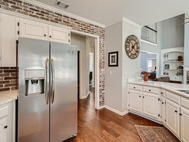 kitchen with stainless steel refrigerator with ice dispenser, white cabinetry, dark wood-type flooring, and brick wall