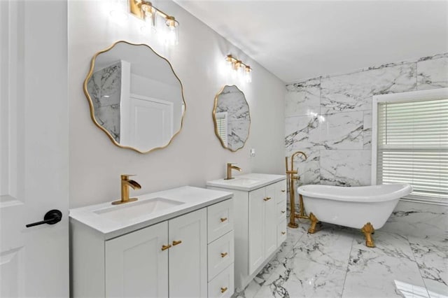 full bath featuring a sink, a freestanding bath, marble finish floor, and two vanities