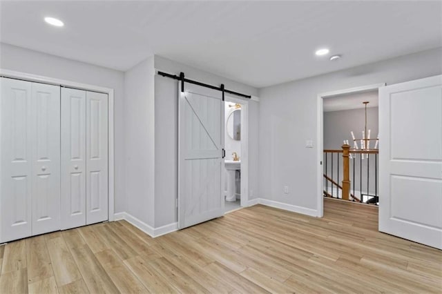 unfurnished bedroom with an inviting chandelier, baseboards, light wood-type flooring, and a barn door