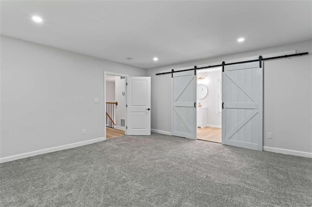 unfurnished bedroom with recessed lighting, a barn door, baseboards, and carpet flooring