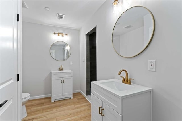 bathroom with visible vents, wood finished floors, two vanities, and a sink