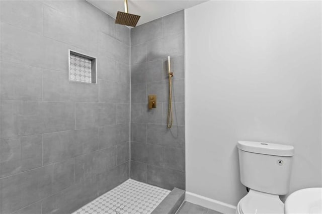 bathroom with toilet, baseboards, and tiled shower