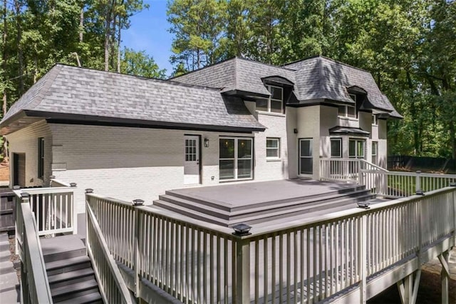 rear view of property with brick siding, a shingled roof, and a deck