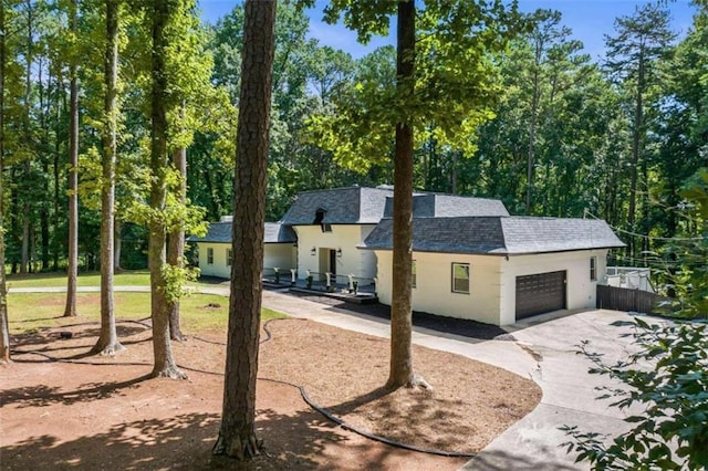 view of front of property with stucco siding, concrete driveway, a garage, and roof with shingles