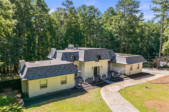 view of front of home with fence, a front yard, roof with shingles, stucco siding, and a chimney