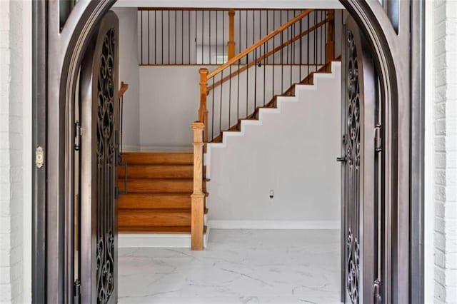 foyer entrance featuring stairway, baseboards, arched walkways, and marble finish floor