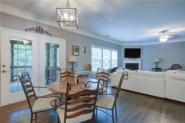 dining space with ornamental molding, dark wood-style flooring, a chandelier, a ceiling fan, and a fireplace
