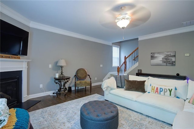 living room with wood finished floors, ornamental molding, ceiling fan, a glass covered fireplace, and baseboards