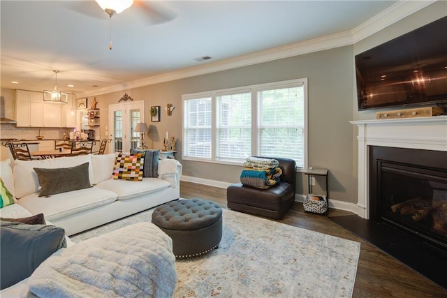 living room with crown molding, dark wood finished floors, a fireplace, baseboards, and a ceiling fan