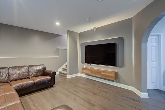 living room featuring baseboards, wood finished floors, stairway, arched walkways, and recessed lighting