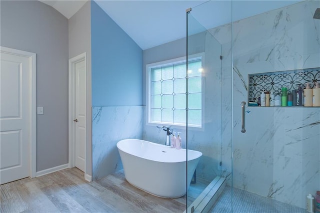 bathroom featuring a marble finish shower, a freestanding bath, tile walls, wood finished floors, and lofted ceiling