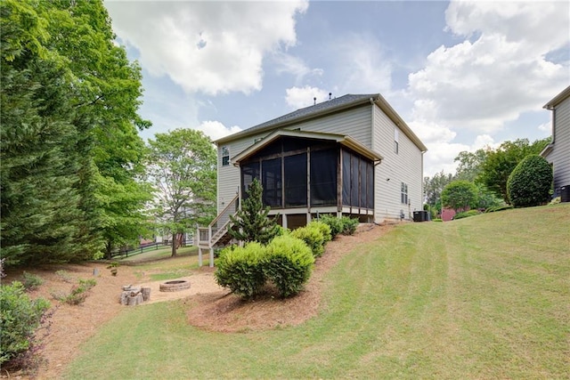 rear view of property featuring a sunroom, a lawn, stairway, a fire pit, and cooling unit