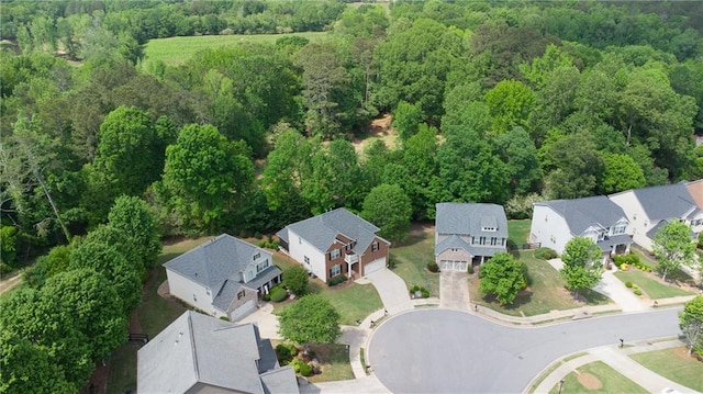aerial view of property and surrounding area featuring a forest and nearby suburban area