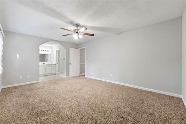 unfurnished bedroom with arched walkways, light carpet, baseboards, and ensuite bath