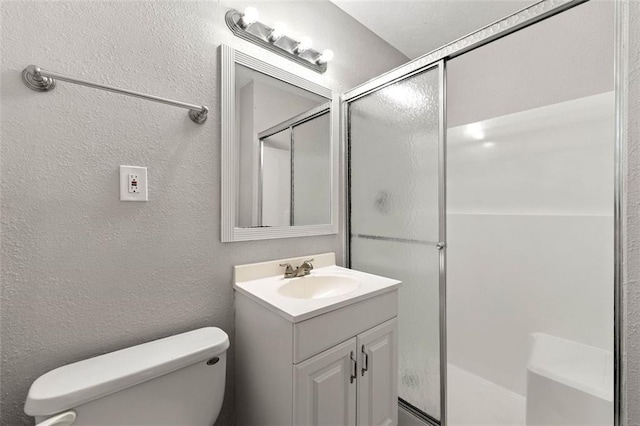bathroom with a textured wall, a shower stall, vanity, and toilet
