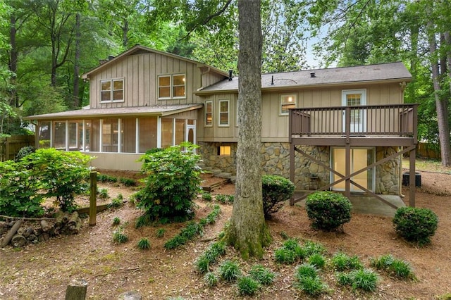 rear view of property featuring a sunroom, board and batten siding, stone siding, a wooden deck, and central air condition unit