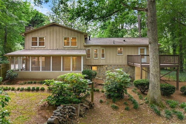 back of house with a chimney, a sunroom, stone siding, a wooden deck, and board and batten siding