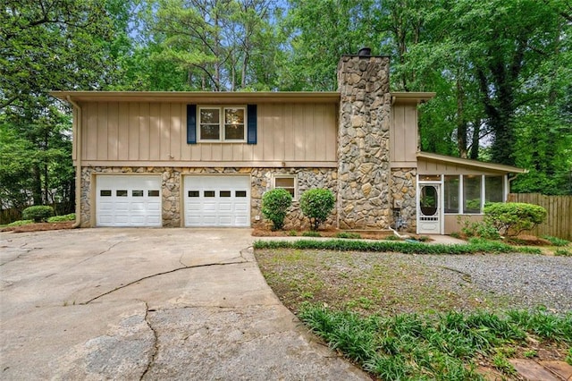 view of front of house featuring concrete driveway, stone siding, a garage, a chimney, and a sunroom