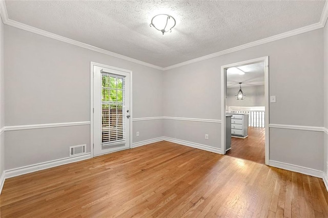 empty room featuring wood finished floors, a textured ceiling, crown molding, and baseboards