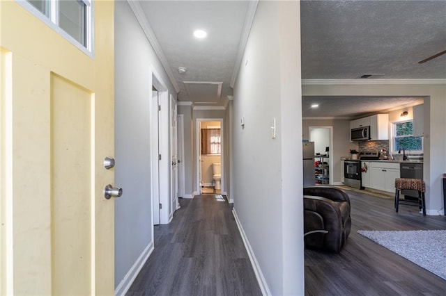 corridor with attic access, baseboards, visible vents, dark wood-type flooring, and crown molding