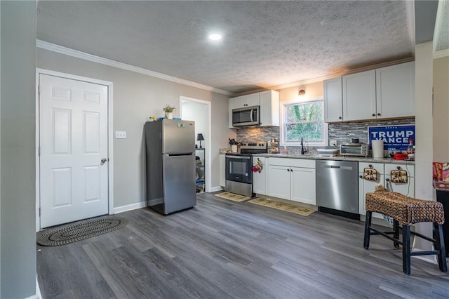 kitchen with dark wood-style floors, appliances with stainless steel finishes, a sink, crown molding, and backsplash