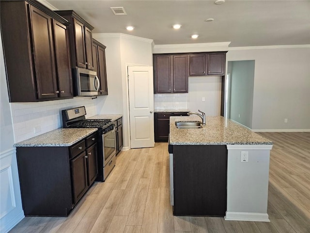 kitchen with visible vents, an island with sink, appliances with stainless steel finishes, light wood-style floors, and a sink