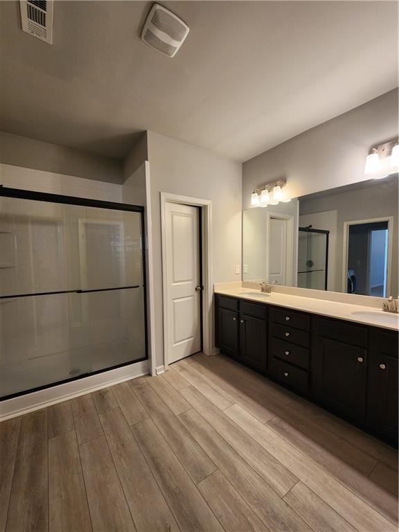 full bathroom with double vanity, visible vents, a sink, a shower stall, and wood finished floors