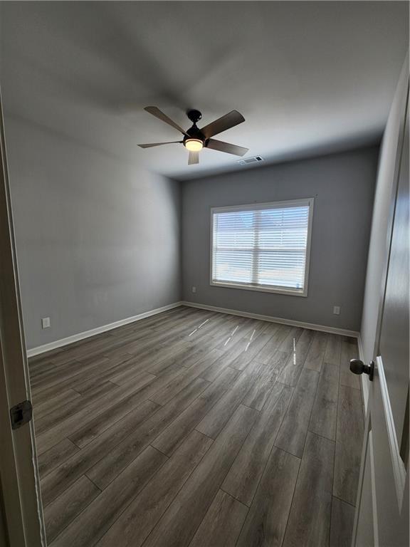 empty room featuring a ceiling fan, baseboards, visible vents, and wood finished floors