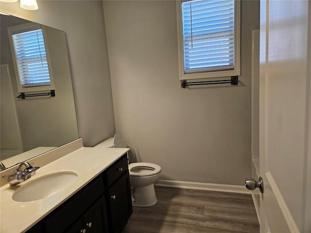 bathroom with toilet, vanity, wood finished floors, baseboards, and a bath