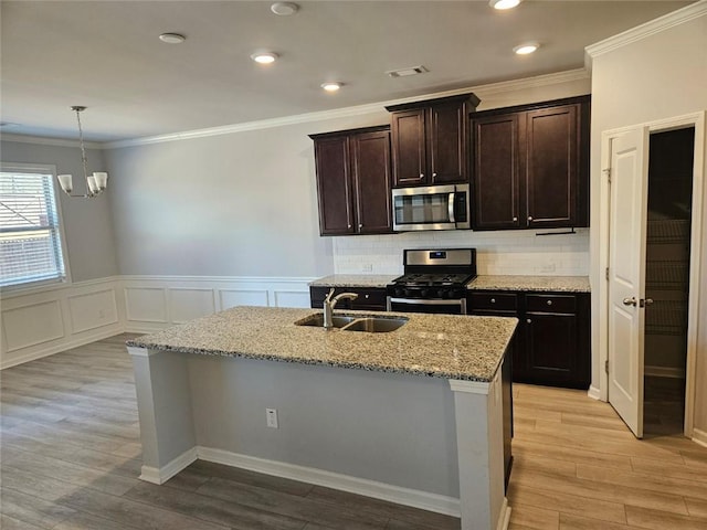 kitchen featuring stainless steel appliances, a sink, light stone counters, and light wood finished floors