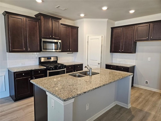 kitchen featuring light stone counters, visible vents, appliances with stainless steel finishes, a sink, and light wood-type flooring