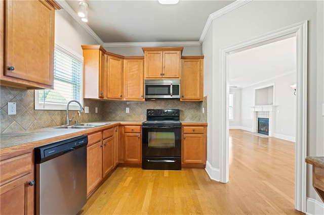 kitchen featuring appliances with stainless steel finishes, a tile fireplace, a sink, and light wood-style flooring