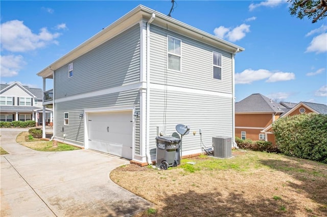 view of side of property with a garage, concrete driveway, central AC unit, and a yard