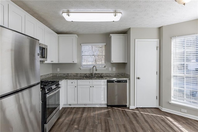 kitchen with sink, dark stone countertops, a textured ceiling, appliances with stainless steel finishes, and white cabinetry