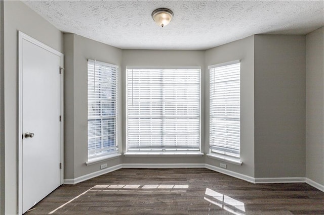 spare room featuring dark wood-type flooring, a healthy amount of sunlight, and a textured ceiling