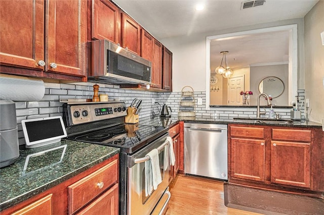 kitchen featuring sink, backsplash, stainless steel appliances, decorative light fixtures, and light wood-type flooring