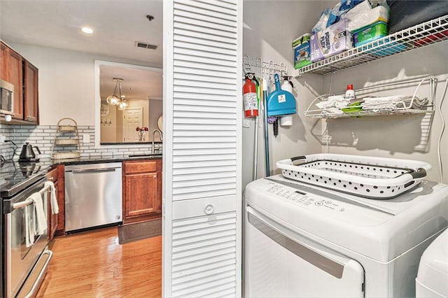 clothes washing area with sink, washer and clothes dryer, and light wood-type flooring