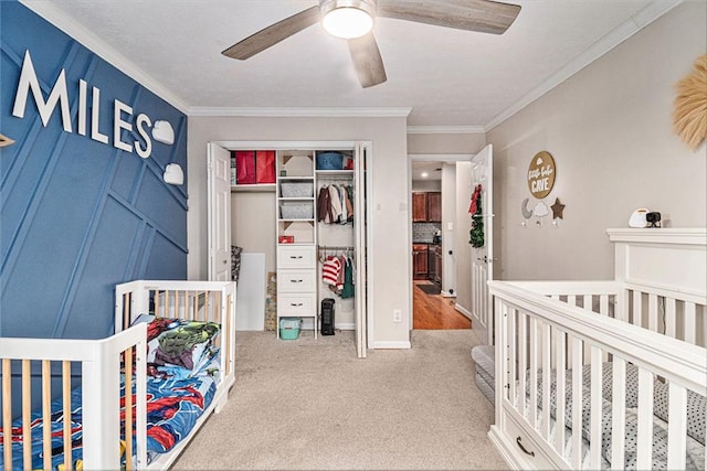 bedroom with ornamental molding, carpet flooring, a closet, a nursery area, and ceiling fan