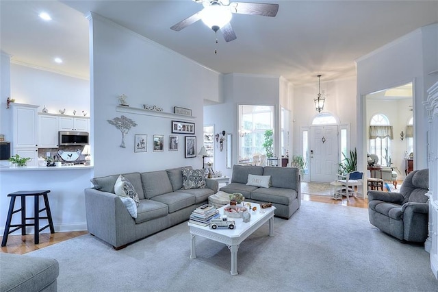 living room with a high ceiling, ceiling fan, crown molding, and light hardwood / wood-style flooring