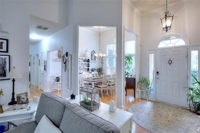 entrance foyer with light wood-type flooring, a towering ceiling, an inviting chandelier, and ornamental molding