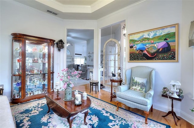 living area featuring crown molding, a raised ceiling, and hardwood / wood-style flooring