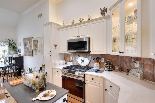 kitchen with vaulted ceiling, appliances with stainless steel finishes, white cabinets, and tasteful backsplash